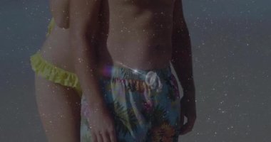 Güneş ışığı, seyahat reklamı için sahilde sarı bikinili bir çift üzerinde mercek parlaklığına neden oluyor. Romantizm, bağlantı, sükunet, rahatlık, açık hava, sükunet, samimiyet.