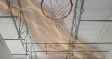 Oyuncu kolu basketbol topuna uzanıp basket potasını tutarken, halat da spor salonunun tavanının altına uzanıyor. Spor, atletizm, aksiyon, ekipman, enerji, performans, hareket