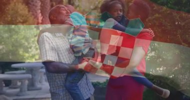 Üst düzey erkek kaldırıcı oğlan ve kadın kızı tutuyor, sağlık için damalı bayrak ile sallıyorlar. Aile, bakım, şefkat, açık hava, boş zaman, bağlantı, uyum.