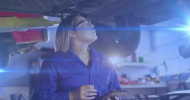 Tamirci kadın, oto garajında kaldırılmış arabayı inceliyor tablet tıkırdatıyor ve tanılama yapıyor. Mekanik, tanı, atölye, sanayi, teknoloji, bakım, hizmet