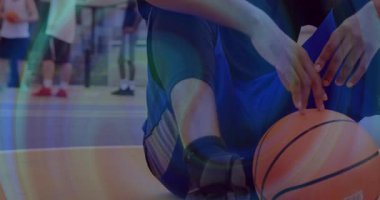 Basketbolcu topu kavrıyor, spor salonunda dizliklerini düzeltiyor, nefes alıyor, antrenmanlara hazırlanıyor. Atletizm, takım çalışması, kararlılık, spor, odaklanma, fitness, yarışma
