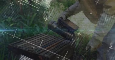 Kıdemli arıcı sigara içiyor, kapağın altına körük pompalıyor, arıları çiftçilik veri grafikleriyle sakinleştiriyor. Apier, tarım, işçilik, doğal, açık hava, sürdürülebilirlik, çevre dostu