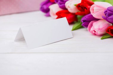 Folded tent card is standing on wooden tabletop, showing flat design with tulip bouquet, copy space. Stationery, floral arrangement, celebration, elegance, event decor, branding, rustic