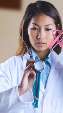 Steteskoplu Asyalı kadın doktor için meme kanseri farkındalığı kurdeleleri. Göğüs kanseri farkındalığı ve sağlık konsepti dijital olarak üretilen video.