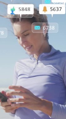 Sahilde akıllı telefonu olan beyaz bir kadın üzerinde sosyal medya veri işleme animasyonu. Küresel fitness, ağlar, hesaplama, dijital arayüz ve dijital olarak oluşturulmuş video işleme kavramı.