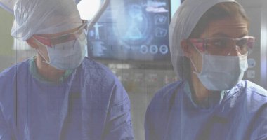 Cerrahi giysi giyen kadın cerrahlar ameliyathanede cerrahi ışıkla monitörde görüntüleniyor. Tıbbi, profesyonel, minimalist, sağlık, hassasiyet, takım çalışması, teşhis
