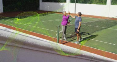 Exchanging high-five senior man and woman standing at net on outdoor tennis court, with rackets. Athletics, recreation, outdoor, activewear, healthy lifestyle, sportsmanship, leisure