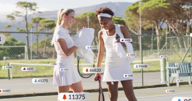 Standing friends in white attire pausing on tennis court, with rackets, bottle, social media icons. Athletic, friendship, leisure, vibrant, outdoor, wellness, competition
