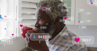 Orta yaşlı Afro-Amerikan bir adam elinde kırmızı bardakla mutfak penceresinden sosyal ikonlarıyla bakıyor. Düşünceli, ev içi, dijital etkileşim, sosyal medya, gündelik, modern, yaşam tarzı