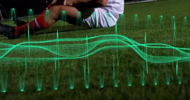 Futbolcu dizini kavrıyor, bacağını göğsüne doğru geriyor, yeşil dalga fırıl fırıl atıyor. Atletik, iyileşme, biyomekanik, eğitim, dayanıklılık, fitness, hareket