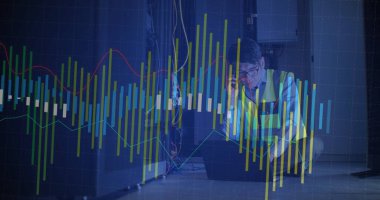 Koreli güvenlik yeleği giymiş çömelmiş bir mühendis sunucu odasında dizüstü bilgisayarını ve telefonunu kontrol ediyor. Teknoloji, veri, bağlantı, siber güvenlik, altyapı, dijital, analitik