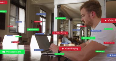 Beyaz tişörtlü bir adam oturma odasındaki masada dizüstü bilgisayarda yüzen etiketlerle çalışıyor. Modern, gündelik, çalışma alanı, minimalist, dijital, iç, işbirlikçi