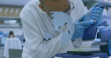 Laboratuvar tezgahında pipetli ve monitörlü mikroplaka takan laboratuvar önlüğü giyen eldivenli bilim adamı. Araştırma, kesinlik, laboratuvar, bilimsel, teknoloji, yenilik, analiz