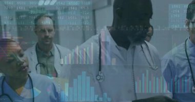 Kıdemli doktor hastane koridorunu durdurdu ve tablet animasyon çizelgelerini ekip verileri gözden geçirirken yürüttü. Tıbbi ekip, sağlık, veri analizi, dijital tablolar, işbirliği, klinik çevre, tıbbi teknoloji