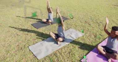 Üç çocuk eğitmen işaretini takip ediyor. İyileşmek için çimenlik alandaki minderlerde yoga egzersizleri yapıyorlar. Açık hava, farkındalık, dinginlik, fitness, rahatlama, uyum, gençlik.