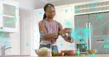 Kadın biber öğütücüsünü kaldırıyor, salata kasesini baharatlıyor. Bu arada akıllı ev simgeleri havada süzülüyor. Akıllı mutfak, birbirine bağlı ev, sağlıklı yaşam, modern tasarım, yaşam tarzı, dijital teknoloji