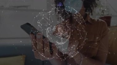 Maskeli kadın akıllı telefonu kanepeye takıyor, dönen ağ küresi projeksiyonunu yapıyor veri ağını görüntülüyor. Teknoloji, bağlantı, dijital, yenilik, iletişim, akıllı cihazlar, modern