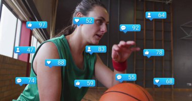 Yeşil formalı kırmızı bileklikli çömelmiş bir sporcu spor salonunda mavi ihbarlarla basketbol topunu kapıyor. Sporcu, spor, spor, spor kıyafeti, spor salonu, hareket, motivasyon