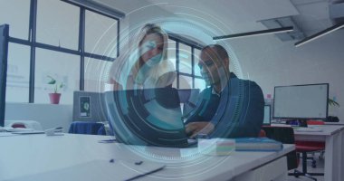 İki ofis çalışanı açık planlı ofiste dizüstü bilgisayar üzerinde çalışıyor. Evrakları ve fabrikası var. İşbirliği, takım çalışması, modernlik, üretkenlik, çalışma alanı, profesyonel, yenilik