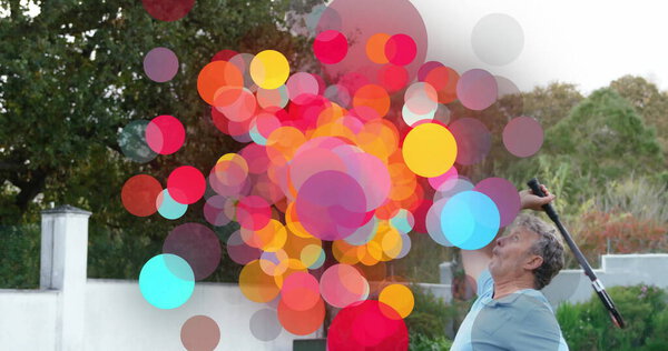 Качающийся старший мужчина в спортивной одежде, поднимающий теннисную ракетку на заднем дворе, с красочными точками, копировальное пространство. Outdoor, leisure, activity, vibrant, fatic, recreation, lifestyle