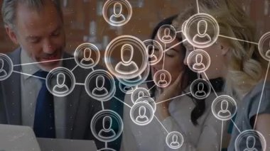 Kamera, ofis toplantısında dizüstü bilgisayarın incelendiğini gösteriyor. Ağ simgeleri kağıt etrafında yüzüyor. İşbirliği, ağ oluşturma, takım çalışması, modern, yenilik, iletişim, iş