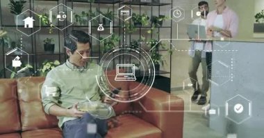 Adam telefonları kaydırıyor yüzen teknoloji simgelerini başlatıyor, iş arkadaşları katılıyor, teknolojiyi tartışıyorlar. İşbirliği, yenilik, dijital, çalışma alanı, iletişim, modern, bağlantı