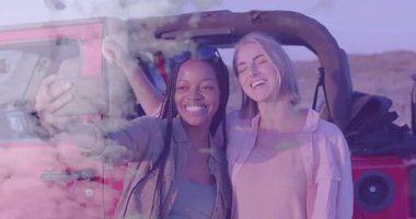 İki bayan arkadaş akıllı telefon kaldırıyor ve kırmızı Jeep 'in yanında selfie çekiyorlar. Yolculuk anılarını yakalıyorlar. Macera, arkadaşlık, açık hava, manzara, günlük, yaşam tarzı, canlı
