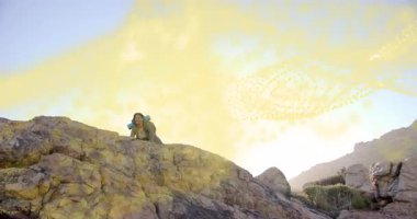 Kaya sürükleyen bir gezgin, tepeye tırmanırken arkasında dönen altın sisli enerjiyi kucaklıyor. Macera, vahşi doğa, keşif, esneklik, başarı, açık hava, dinamik