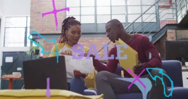 Meslektaşlar sarı klasördeki belgeleri incelerken koltukta dizüstü bilgisayarla kahve içiyorlar. İşbirliği, gündelik, modern, endüstriyel, takım çalışması, profesyonel, çalışma alanı