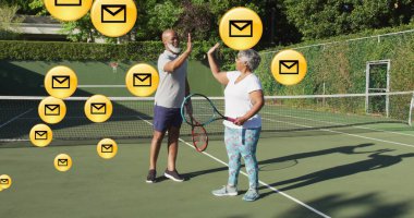 Tenis kortunda tenis kıyafetleri giymiş, zarf simgeleriyle beşlik çakan bir adam ve son sınıf İspanyol bir kadın. Atletizm, takım çalışması, aktif, motivasyon, açık hava, fitness, yoldaşlık