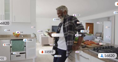 Ekose gömlekli adam modern mutfak adasına yaslanmış elinde akıllı telefon, yüzen sosyal ölçülerle. Çağdaş, gündelik, yaşam tarzı, teknoloji, iç mekan, mimari, bağlantı