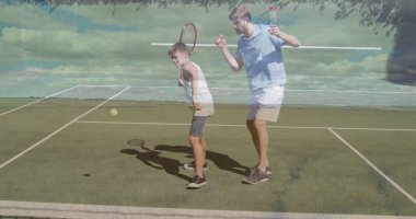 Tenis antrenmanı, tenis kıyafetleri içinde baba-oğul ikilisi tenis kortunda raket sallıyor, top ve ağla. Atletizm, aile, açık hava, spor, eğlence, etkinlik, canlılık