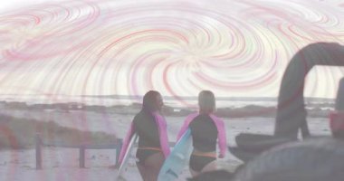 Güneş batarken iki dişi sörfçü okyanusa doğru pastel kaplamayla yürüyorlar. Plaj, okyanus, günbatımı, dalgalar, yoldaşlık, macera, huzur