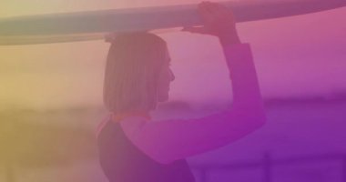 Gün batımında sörf tahtası kaldıran sörfçü kadın, sahil korkuluklarında sörf için tutunmaya çalışıyor. Sahil, sahil, açık hava, yaşam tarzı, atletik, macera, uyum.