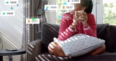 Elinde akıllı telefondan uyarı alan kupa tutan bir kadın sosyal medya bilgilendirme simgelerine neden oluyor. Rahatlama, refah, dijital iletişim, modern ev, rahat atmosfer, rahatlık, sosyal etkileşim