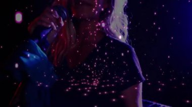 Sahnede müzik için şarkı söylerken mikrofonu çeken sanatçı parlayan parçacık kaplamasını tetikliyor. Performans, vokal, sahne, ışıklandırma, dijital sanat, eğlence, canlı