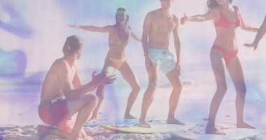 Kumsalda sörf tahtasında denge çalışması yapan altı kişilik bir grup. Parlak mayo giyiyorlar. Eğlence, takım çalışması, kıyı, enerjik, canlı, yaz, etkinlik