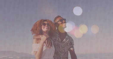 Okyanusun kıyısında duran omuzsuz, çiçekli tişört ve güneş gözlüğü giyen gülümseyen bir çift. Aşk, eğlence, doğal, açık hava, yaşam tarzı, dinginlik, mutluluk.