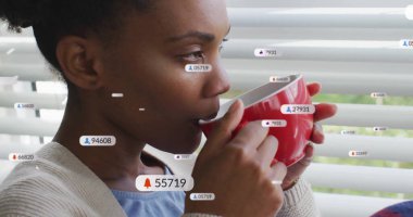 Evde elinde kırmızı bardakla dolaşan dijital uyarı simgeleriyle jaluzi tutan bir kadın. Rahatlama, rahatlık, farkındalık, dijital, ev vücudu, rahatlık, çağdaş