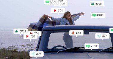 Kumlu plajın tepesinde yüzen sosyal medya simgeleriyle kareli battaniye tutan bir kadın. Macera, yaşam tarzı, açık hava, rahatlama, rahatlama, iletişim, modern