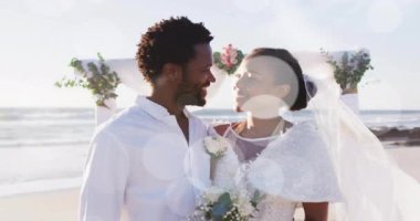 Düğünde kumsalda gülümseyen mutlu Afro-Amerikan gelin ve damadın üzerindeki ışık noktalarının animasyonu. Romantizm, aşk, tatiller ve evlilik, dijital olarak üretilen video.