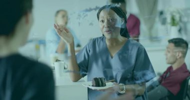 Hemşire dinlenme odasında iş arkadaşlarıyla pasta sunarken ve gülerken sağlık verileri üst üste geliyor. Sağlık, takım çalışması, yoldaşlık, dijital, modern, profesyonel, gündelik