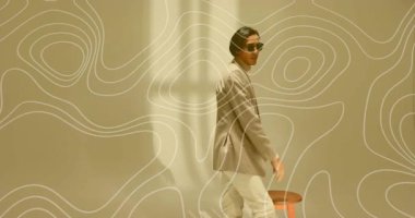 Erkek model çerçeveye giriyor ve tabureye yaslanıyor. Moda için ceketi ayarlıyor. Çizgiler arasında duruyor. Şık, kendine güvenen, zarafet, minimalizm, profesyonellik, modern, çağdaş