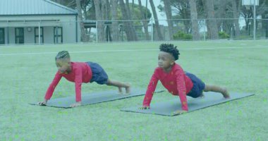 İki çocuk siyah paspaslara bastırıyor ve gövdelerini kobra pozisyonuna getiriyorlar. Fitness, gençlik, açık hava, çeviklik, güç, takım çalışması, canlılık