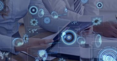 İş arkadaşları ofis masasındaki doküman ve tableti kalem, su ve holografik arayüzle inceliyorlar. Gelecekçi, yenilikçi, takım çalışması, dijital, işbirliği, modern, teknoloji