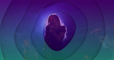 Sahnede elinde mikrofonla şarkı söyleyen sarışın kadın solist. Renkli ışıklar puslu. Konser, performans, sahne, eğlence, görsel efektler, müzik, müzisyen