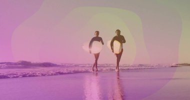 Dalgıç kıyafeti giyen, kumlu sahil boyunca beyaz sörf tahtaları taşıyan, aynalı ıslak kum taşıyan bir çift. Sahil şeridi, boş zaman, macera, açık hava, uyum, sükunet, rahat giysi