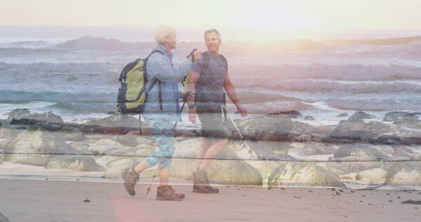 Using trekking poles couple hikers walking along beach at sunrise, with backpacks. Adventure, exploration, coastline, serenity, outdooractivity, travel, nature