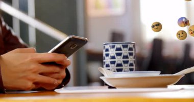 Bu video, bir restoranda cep telefonunu kullanan güzel bir kadını gösteriyor. Arka planda sarı 3D emoji yüzleri ve sola doğru hareket eden çeşitli ifadeler var..