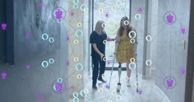 Hasta kadın bakıcı elini sıkıyor ve fayans koridoru boyunca yürüme terapisine başlıyor. Rehabilitasyon, erişilebilirlik, iyileşme, fizyoterapi, güçlendirme, destek, esneklik